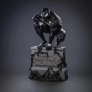 May include: Black and white statue of Venom, a Marvel Comics superhero, crouching on a tombstone. The tombstone reads "Here Lies Eddie Brock".