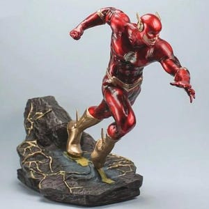 Op de afbeelding: Een rood en gouden The Flash-actiefiguur dat op een getextureerde zwarte basis rent. De figuur is geposeerd in een dynamische renpositie met één arm uitgestoken.