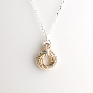 May include: A silver chain necklace with a gold and silver intertwined ring pendant.