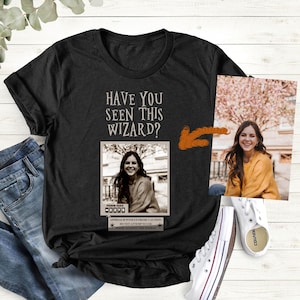 May include: A black t-shirt with the text "Have you seen this wizard?" and a vintage-style wanted poster featuring a woman with long brown hair. The poster has the text "Prisoner 8484" and "Approach with extreme caution. Do not attempt to flee." The t-shirt is paired with blue jeans and white sneakers.