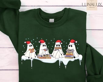Puede incluir: Sudadera verde oscuro con un diseño de cuatro fantasmas blancos con gorros de Papá Noel leyendo libros. Los fantasmas están sobre una superficie nevada, con copos de nieve encima. La sudadera tiene cuello redondo y mangas largas.