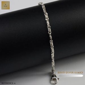 May include: A silver chain bracelet featuring a repeating pattern of interconnected links with textured, wrapped detailing. The bracelet includes a lobster claw clasp and is labelled as solid silver with a weight of 11.90 grams, reference number 4.