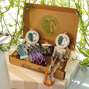 Könnte beinhalten: Ein brauner Karton mit einem grünen Logo, auf dem "Climbing Vine Gear Shop" steht. Die Box enthält verschiedene Kletterausrüstung, darunter Karabiner, Seil und eine kleine Tasche.