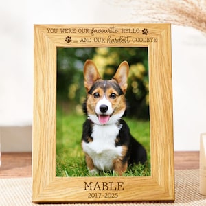 Puede incluir: Marco de fotos de madera con una foto de un perro Corgi. El marco tiene grabado el texto "YOU WERE OUR favourite hello ... AND OUR hardest goodbye." El nombre del perro, "MABLE", y los años "2017-2025" también están grabados.