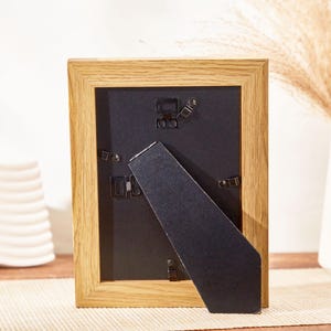 May include: A wooden picture frame with a black mat and a black easel stand. The frame is made of natural wood with a light brown finish.