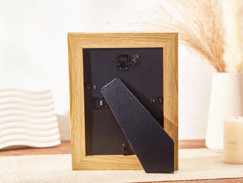 May include: A wooden picture frame with a black mat and a black easel stand. The frame is made of natural wood with a light brown finish.
