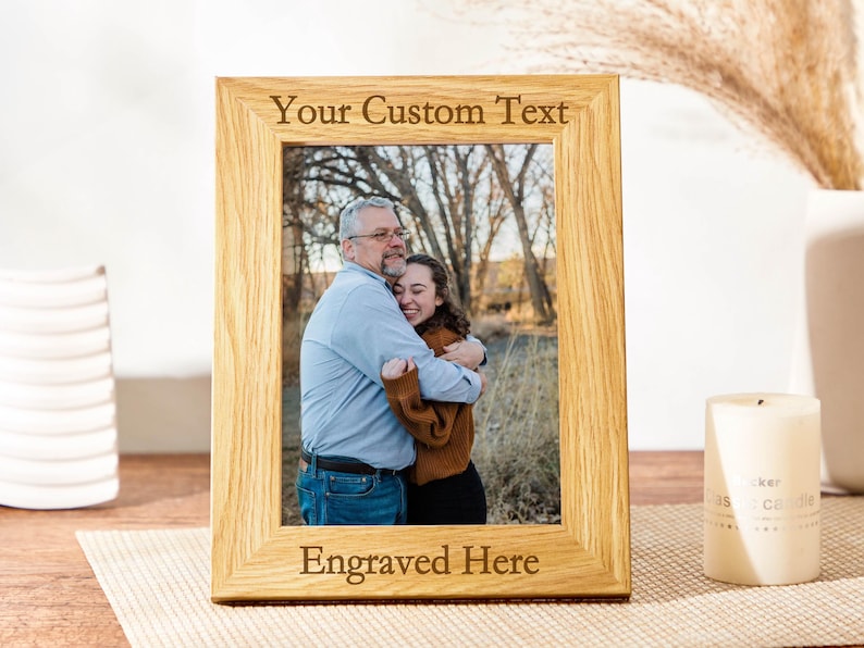 May include: A wooden picture frame with a photo of two people hugging. The frame has a space for engraving with the text "Your Custom Text" and "Engraved Here".