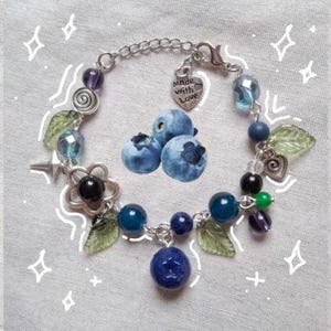 May include: A silver charm bracelet with a variety of charms, including leaves, flowers, stars, and blueberries. The bracelet also has a heart charm that says "Made with Love".