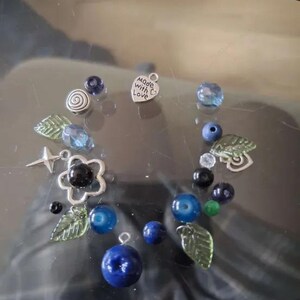 May include: A collection of blue and green glass beads, silver charms, and a silver heart charm with the text "Made with Love".