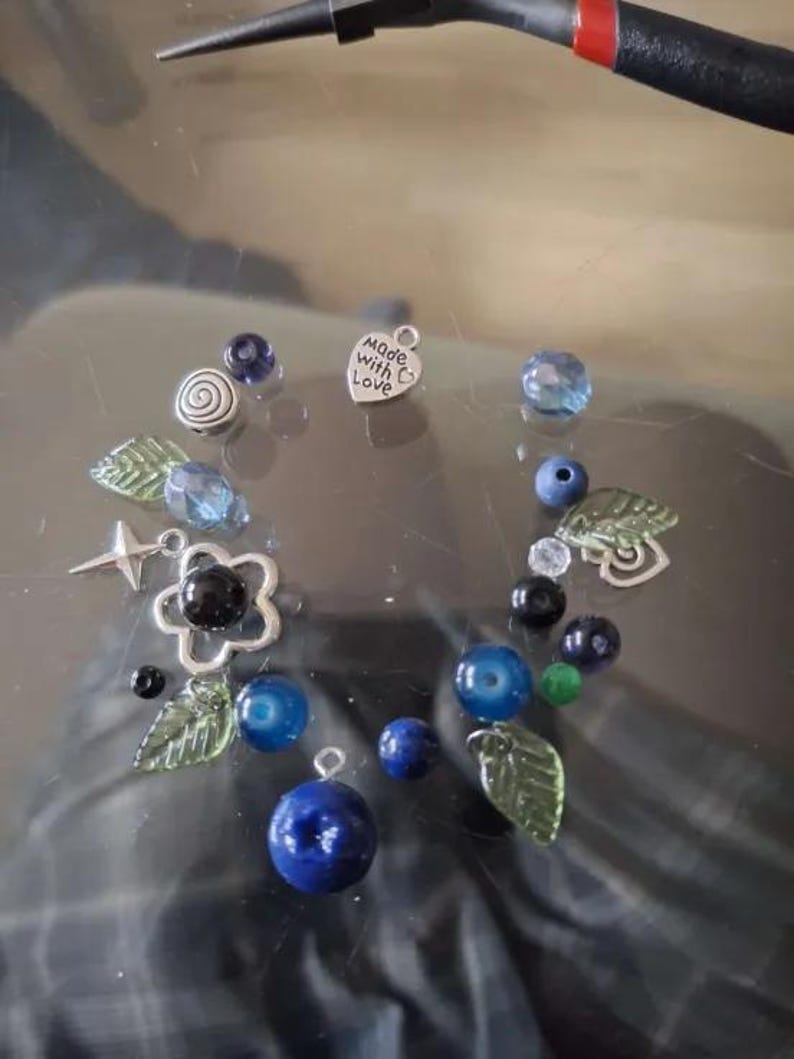 May include: A collection of blue and green glass beads, silver charms, and a silver heart charm with the text "Made with Love".