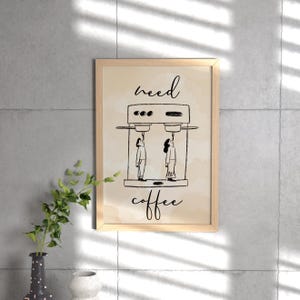 Könnte beinhalten: Ein gerahmter Druck mit beigefarbenem Hintergrund und einer schwarzen Tintenillustration von zwei Personen, die unter einer Kaffeemaschine stehen. Der Text "need coffee" ist in schwarzer Tinte geschrieben.