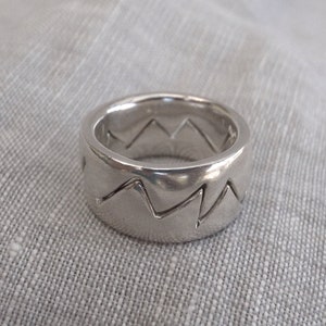 May include: A silver ring with a zig-zag pattern around the band.