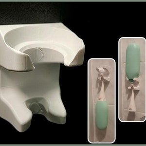 Może przedstawiać: Biały plastikowy uchwyt ścienny z dwoma haczykami do zawieszania przedmiotów, takich jak szczoteczka do zębów lub butelka mydła. Uchwyt ma zakrzywiony górny element do trzymania butelki. Uchwyt jest pokazany z dwoma butelkami mydła, jedną zieloną i jedną białą, wiszącymi na haczykach.