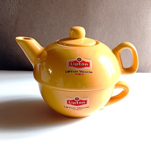 Può includere: Servizio da tè in ceramica gialla con una teiera con coperchio e una tazza abbinata. Il set è marchiato con il logo "Lipton" e le parole "Lipton Yellow". La teiera ha un beccuccio e un manico, e la tazza ha un manico.