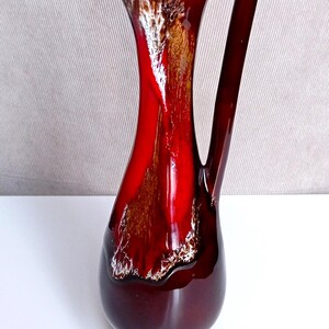 Peut inclure: Une cruche en céramique rouge brillante avec une poignée unique. La cruche a une base sombre et une ouverture évasée. L'intérieur présente un motif or et blanc. Un objet décoratif pour la maison.