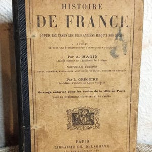 Peut inclure: Livre ancien intitulé "Histoire de France", avec une couverture beige usée et un dos noir. La couverture présente du texte orné et un emblème décoratif, indiquant son caractère historique.