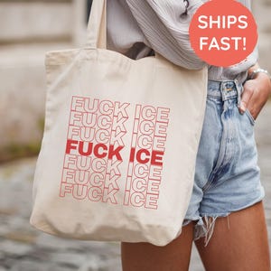 May include: A beige canvas tote bag with the words "FUCK ICE" repeated in red. The bag is being held by a person wearing a light gray shirt and denim shorts. A red circle with the words "SHIPS FAST!" is visible.