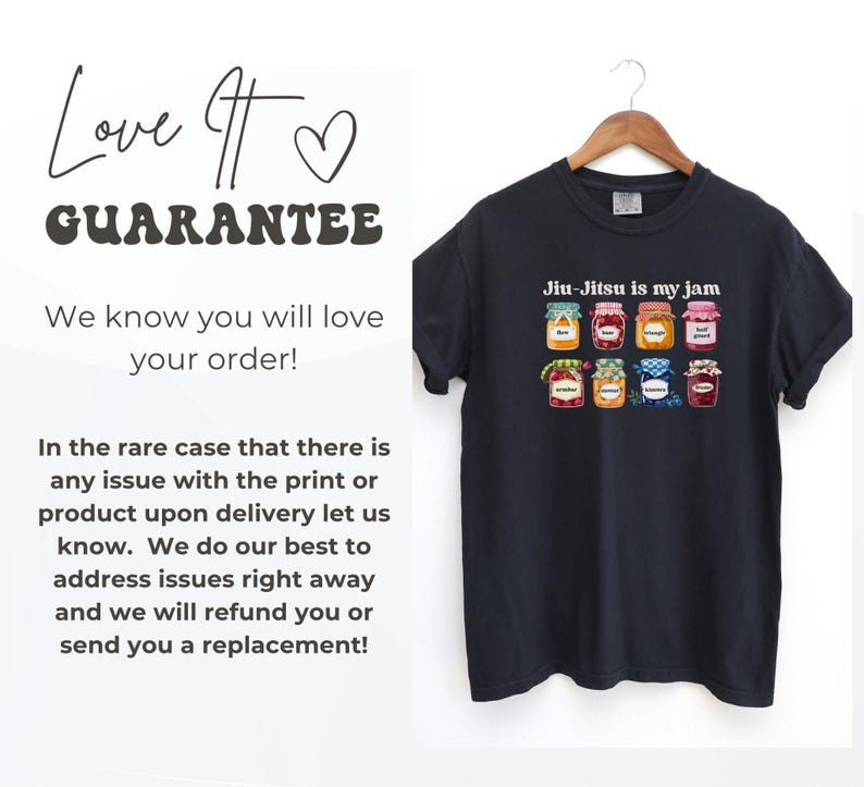 K&ouml;nnte beinhalten: Ein dunkelgraues Kurzarm-T-Shirt mit einem Grafikdruck von acht bunten Marmeladengl&auml;sern und dem Text "Jiu-Jitsu is my jam" dar&uuml;ber. Das T-Shirt h&auml;ngt auf einem Holzkleiderb&uuml;gel vor einem schlichten wei&szlig;en Hintergrund.