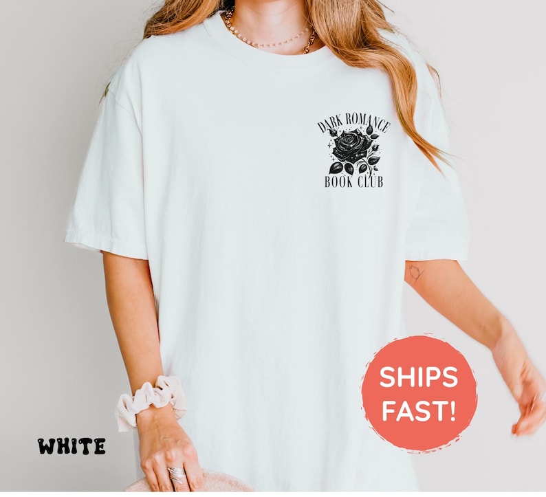 May include: A white short-sleeved t-shirt featuring a black graphic on the upper left chest. The graphic depicts a rose with leaves and the text "DARK ROMANCE BOOK CLUB" arched above and below the flower in a serif font style.