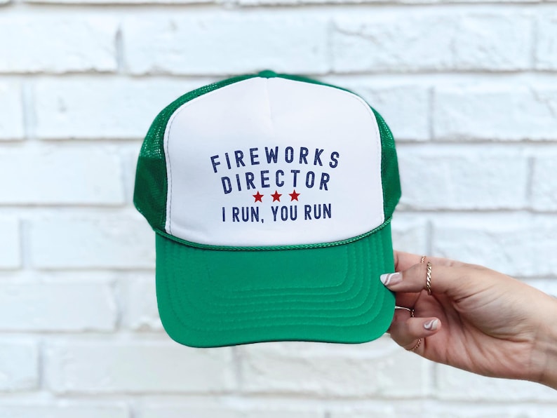May include: Green and white trucker hat with the text "FIREWORKS DIRECTOR I RUN, YOU RUN" in navy blue. The hat has a green brim and mesh back, with three red stars below the word "DIRECTOR".