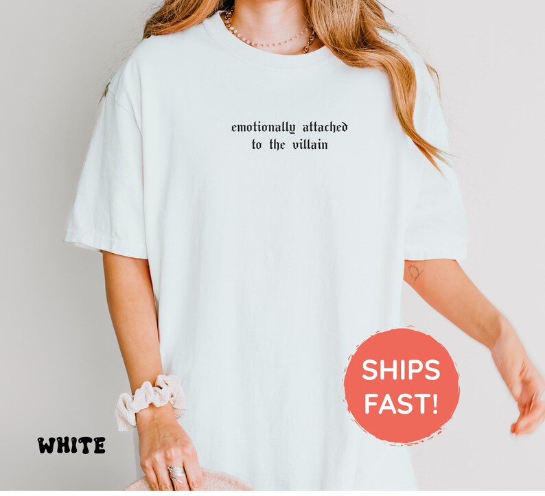 May include: White t-shirt with the text "emotionally attached to the villain" in black gothic font. The shirt is a relaxed fit and has short sleeves. The word "WHITE" is printed in a black font at the bottom left.