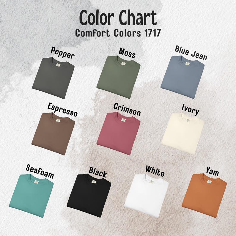 May include: A color chart for Comfort Colors 1717 t-shirts displaying nine folded shirts in various colors labeled Pepper, Moss, Blue Jean, Espresso, Crimson, Ivory, Seafoam, Black, White, and Yam, arranged in a grid on a textured background.
