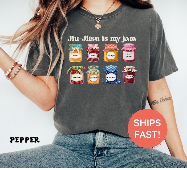 K&ouml;nnte beinhalten: Ein anthrazitfarbenes T-Shirt mit dem Text Jiu-Jitsu is my jam &uuml;ber einer Grafik von acht bunten Gl&auml;sern. Jedes Glas ist mit einem bestimmten Begriff beschriftet: flow, base, triangle, half guard, armbar, mount, kimora und frame.