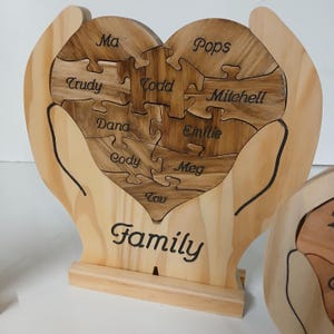 May include: Wooden heart-shaped puzzle with the word "Family" engraved below. The puzzle pieces are labeled with names, including "Ma", "Pops", "Trudy", "Todd", "Mitchell", "Dana", "Emilie", "Cody", "Meg", and "Tov".