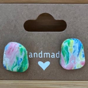 May include: Handmade stud earrings with a colorful, marbled design in shades of pink, green, blue, and yellow. The earrings are displayed on a brown card with the word "handmade" and a heart symbol.