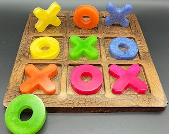 Puede incluir: Un colorido juego de tres en raya con un tablero de madera y piezas de resina vibrantes. El juego presenta X y O amarillas, naranjas, azules, verdes y rosas. El tablero tiene un acabado marrón texturizado.