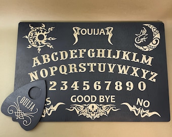 May include: A black wooden Ouija board with gold lettering and symbols. The board features the alphabet, numbers 1-9 and 0, the words "yes", "no", "good bye", and a planchette.