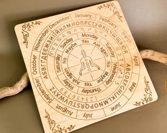 May include: Wooden circular divination board with a central figure in a meditative pose. The board features a circular alphabet, numbers, days of the week, months of the year, and yes/no options. The board is designed for use with a pendulum or other divination tool.