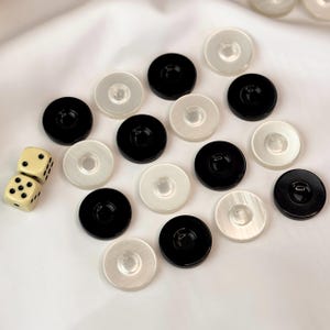 May include: A collection of backgammon game pieces and dice. The pieces are round, with alternating black and white colors. The dice are off-white with black dots. The game pieces are arranged on a white surface.
