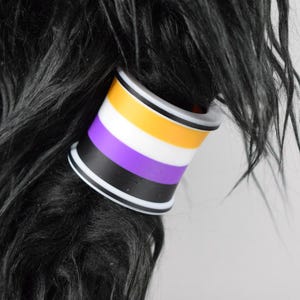May include: A black and white hair tie with purple, yellow and white stripes. The hair tie is made of a soft, flexible material and is designed to hold hair in place.