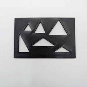 May include: A black rectangular object with several triangular cutouts. The cutouts reveal a white background, creating a geometric design. The object has a textured surface, and the triangles are of varying sizes and orientations.