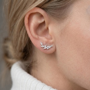 May include: A silver-toned ear climber earring featuring a cluster of marquise and round-cut clear stones arranged in a curved, leaf-like pattern that follows the natural shape of the earlobe, secured with a post backing.