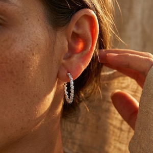 May include: A silver hoop earring with a textured, bumpy surface. The earring is circular in shape and features a repeating pattern of small, raised metallic segments along the entire outer edge of the hoop, creating a distinct, tactile appearance.