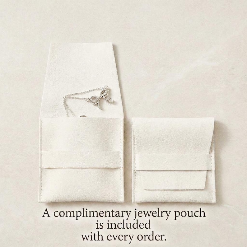 May include: Two off-white jewelry pouches, one open to reveal a silver necklace. The necklace has a bow and charm pendant. The text at the bottom reads, "A complimentary jewelry pouch is included with every order."