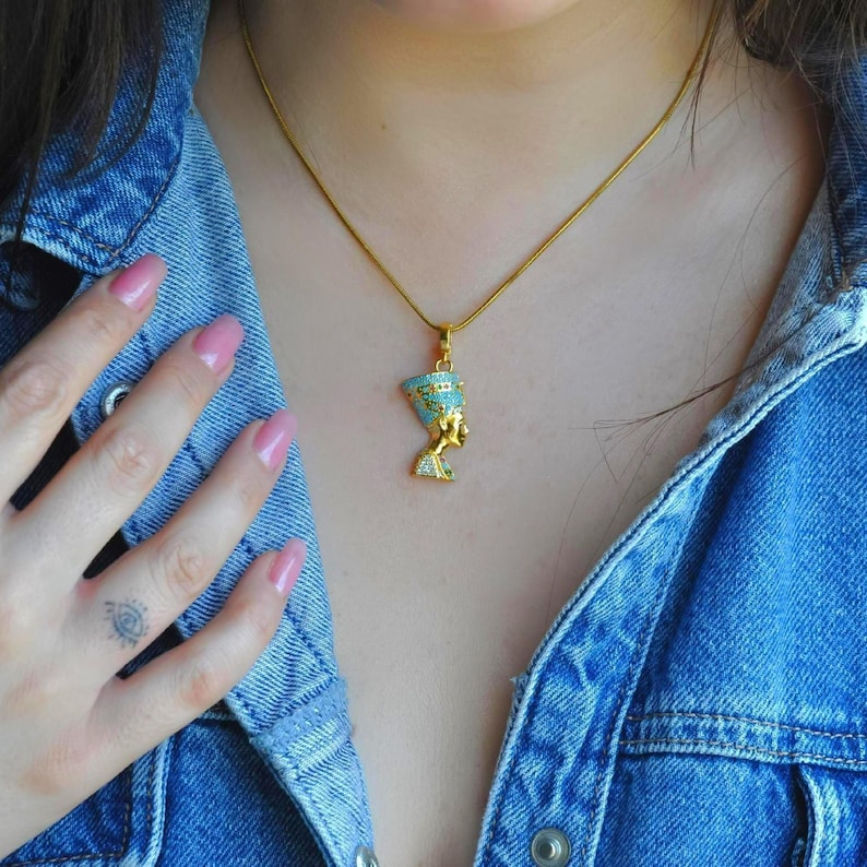 A female model wearing the handmade 24K gold plated Nefertiti necklace with turquoise gemstones to show the perfect scale and fit. This elegant necklace for women is a popular choice for anniversary gifts for her or a high quality birthday gift for mom. The vibrant Egyptian queen necklace sits beautifully on the neck making it a versatile gift for her.
