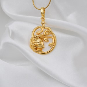 Puede incluir: Un collar con colgante dorado con un dise&ntilde;o de Medusa. El colgante muestra el perfil de Medusa con serpientes, suspendido de una fina cadena dorada. El collar se presenta sobre tela blanca y sedosa.