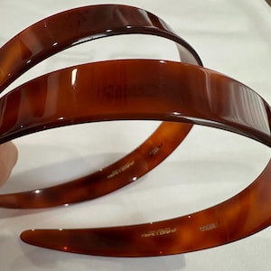 May include: Two brown plastic headbands. The headbands are smooth and shiny. The text "Made in Italy" is printed on the inside of the headbands.