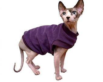 May include: A hairless cat wearing a purple fleece sweater. The cat is standing on a white background.