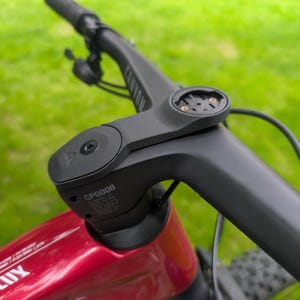 Peut inclure: Gros plan sur un guidon de vélo noir avec un support intégré pour un ordinateur de cyclisme. Le guidon est fixé à un cadre de vélo rouge. L'arrière-plan est de l'herbe verte floue.