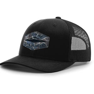 May include: Black trucker hat with a mesh back and a curved brim. The front features a patch with a UFO design and the text "SHOW ME YOUR BUNKERS" in white and blue.
