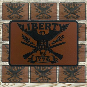 May include: A collection of brown leather coasters and a larger mat featuring a black eagle emblem with the words "LIBERTY" and "OR DIE". The year "1776" is also displayed. The coasters have a wood grain background.