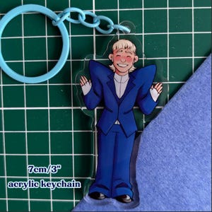 May include: Acrylic keychain with a cartoon figure in a blue suit. The keychain has a light blue ring and chain. The text "7cm/3" acrylic keychain" is printed at the bottom. The keychain is approximately 7 cm in height.
