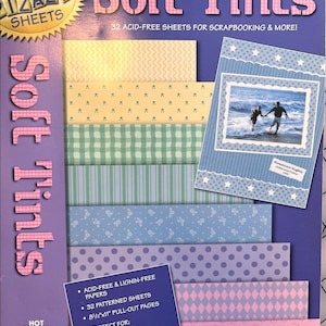 May include: A package of "Soft Tints" scrapbook paper sheets. The cover is purple with the words "Soft Tints" in pink. Inside are patterned sheets in pastel colors, including yellow, green, blue, and pink. The package includes 32 acid-free sheets.