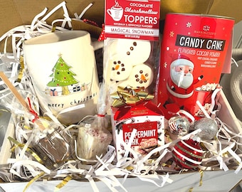 May include: A Christmas-themed gift box filled with festive treats. Includes a mug with a Christmas tree design and the words "merry christmas", marshmallow toppers, candy cane cocoa powder, peppermint bark, and ornaments.