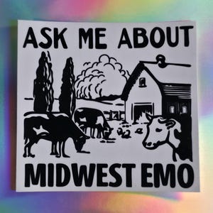 May include: A square white sticker featuring a black ink-style illustration of a farm scene with a barn, two cows, and trees. The text "ASK ME ABOUT" is printed in black at the top, and "MIDWEST EMO" is printed in black at the bottom of the sticker.
