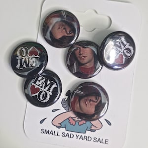 May include: A set of six round pinback buttons. Three buttons feature a person's face, and the other three have the letters "EMO" with a heart. The buttons are on a white card with the text "SMALL SAD YARD SALE".